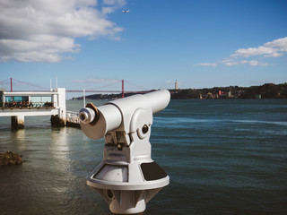 White coin binocular on viewpoint against city river with embankment in sunlight in Lisbon, Portugal