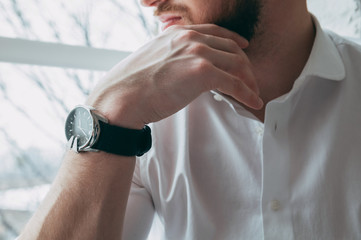 Cropped view of the boss, propping his hand on the chin, on his arm is an expensive and stylish watch, against the background of the window, the concept