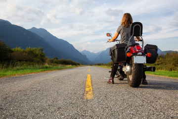 Fototapeta premium Woman riding a motorcycle on a scenic road surrounded by Canadian Mountains. Taken in Pitt Meadows, Greater Vancouver, BC, Canada.
