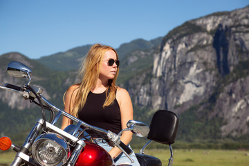Fototapeta na wymiar Young woman on a motorcycle in nature during a vibrant sunny summer day. Taken in Squamish, North of Vancouver, British Columbia, Canada.