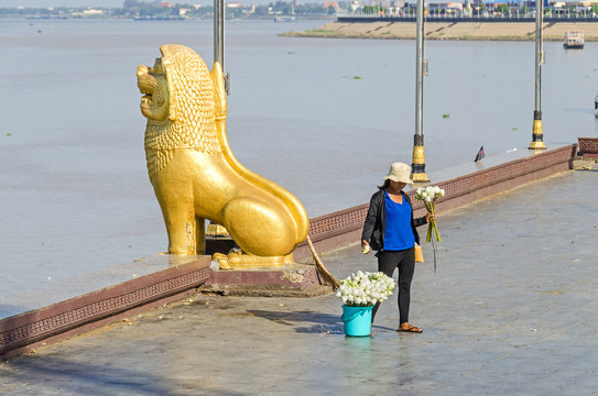 Preah Sisowath Quay in Phnom Penh with the statue of the guardian lion and a woman selling lotus flowers