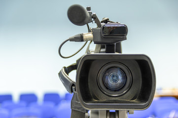Front view of video camera with blurred hall background, selective focus.
