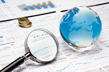 Glass Globe, Magnifying Glass And Coins On Financial Reports