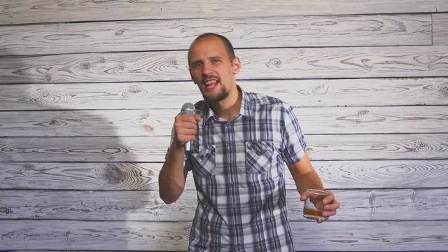 Drunk man holding a glass of alcohol and singing on a microphone on the party
