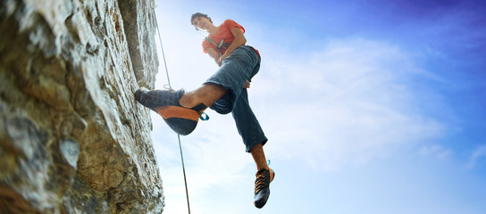 male rock climber on the cliff against a blue sky