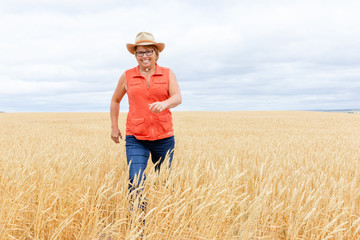 Naklejka na ściany i meble caucasian woman laughing as she walks in a wheat field