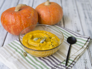 Pumpkin soup with cream and pumpkin seeds on old white wooden table, on a background of two orange pumpkin . Сopy space, Close up