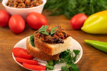 Appetizer of bread with stewed sliced vegetables on the background of whole ripe tomatoes, peppers and dill leaves.