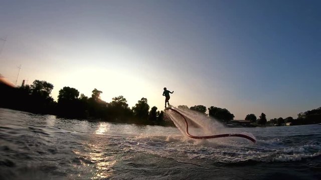 Flyboarder doing tricks flying slow motion Flyboarding wide shot video on sunset backlight