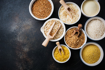 Variety of cereal flakes rice, millet, buckwheat, oatmeal. Superfood in white ceramic bowls on dark old   concrete background. Top view.