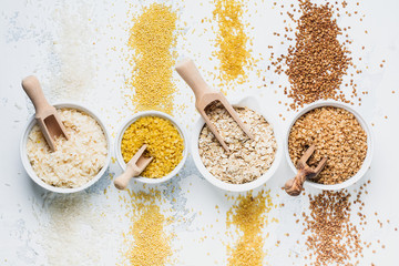 Variety of cereal flakes rice, millet, buckwheat, oatmeal. Superfood in white ceramic bowls on light wooden background. Top view.