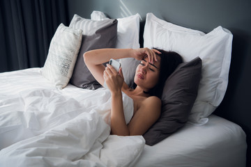Image of frustrated upset woman 20s with dark hair lying in bed on white pillow after sleep and...
