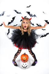 Little Girl with a demon devil costume dressed up in black red dress and red devil horns for pumpkin patch and halloween party, posing with happy smiling pumpkins jack o lantern and black bats