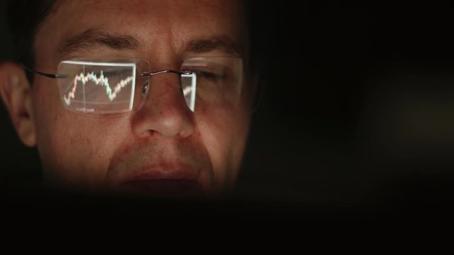 REFLECTION: Face of trader in an eyeglasses looking a graphs in a the night