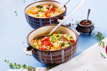 Soup with small pasta, vegetables and pieces of meat in  bowl on  blue table. Italian food.