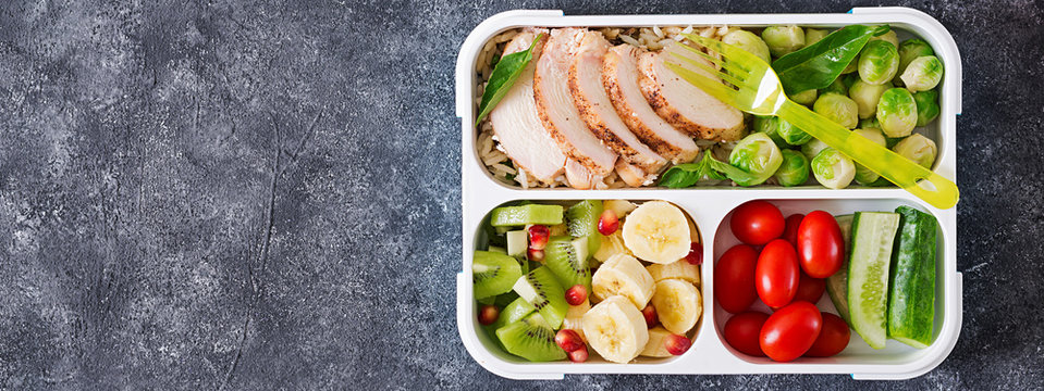 Healthy green meal prep containers with chicken fillet, rice, brussels sprouts, vegetables and fruits overhead shot with copy space. Dinner in lunch box. Top view. Banner. Flat lay