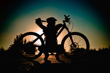 Fototapeta na wymiar Silhouette of a girl with a bicycle at sunset in the summer