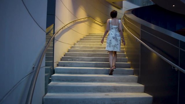 a young attractive woman in a flower and butterfly dress walks up the stairs at a leisurely pace then speeds up. background is a modern building