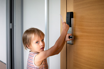 Little boy trying to open doors with card lock at the hotel, holding by hinge