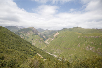Fototapeta na wymiar Mountain gorge of Georgia, top view of the green hills with a cleft on the Georgian military road. The sky is covered with cloudy grey clouds, the gorge is in fog.