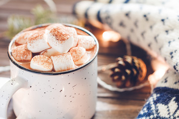 Hot cocoa with marshmallow in a white ceramic mug among winter things on a wooden table. The concept of cozy holidays and New Year.