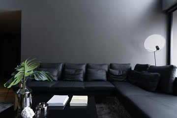 Cozy black leather sofa corner in the living room with gray color painted on the wall and black...