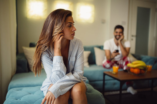 Young brunette is jealous because her boyfriend is smiling and sending text messages while sitting behind her back