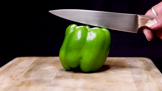 A well focused SLOWMOTION shot of a capsicum getting cut in half by a knife stroke on a wooden table with black background