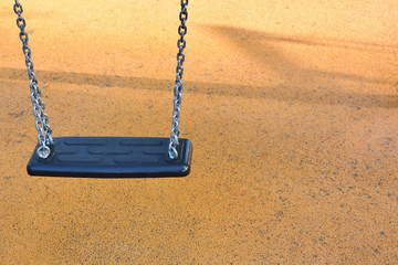 Black empty chain swing seat for children on soft protective coating background with copy space for text in outdoor playground.