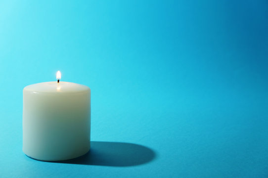 White candle burning on blue backgound