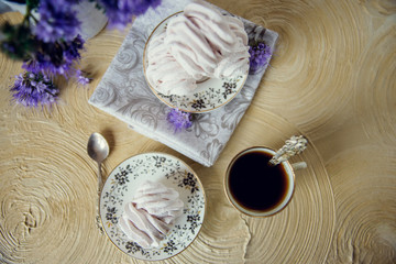 Fototapeta na wymiar Homemade marshmallow on a saucer with appliances and a Cup of coffee, on a light background with purple flowers. The concept of a cozy autumn dessert.