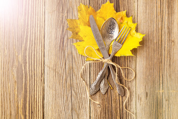 Autumn dinner place setting for Thanksgiving holiday with colorful maple leaves on rustic wooden boards