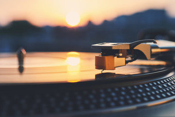 Turntable vinyl record player on the background of a sunset over the lights city. Sound technology...