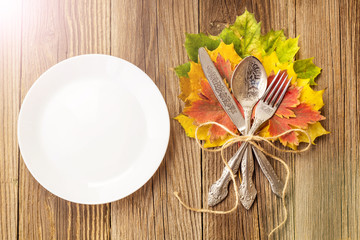 Thanksgiving dinner plate with fork, knife and autumn leaves on rustic wooden table background. Top view, copy space
