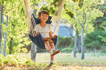 Autumn greeting card with place for your text. A happy boy sits in a comfortable blue hammock that...