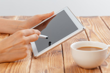 Close-up of young female hands holding digital tablet and drinking morning macchiato.