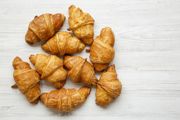 Freshly baked golden croissants on white wooden table, top view. Copy space.