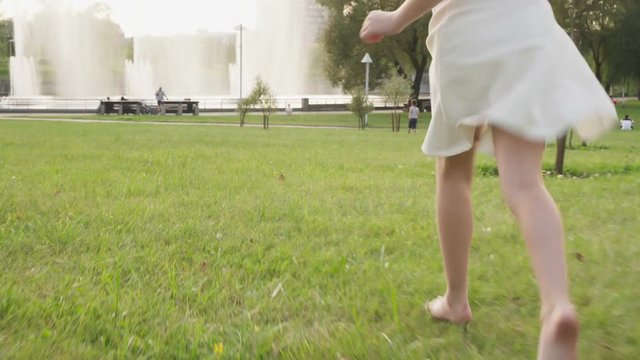 Bare feet of little girl running on grass in summer park