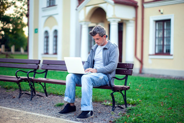 Fototapeta premium Young man with laptop sitting in the park. People, technology concept