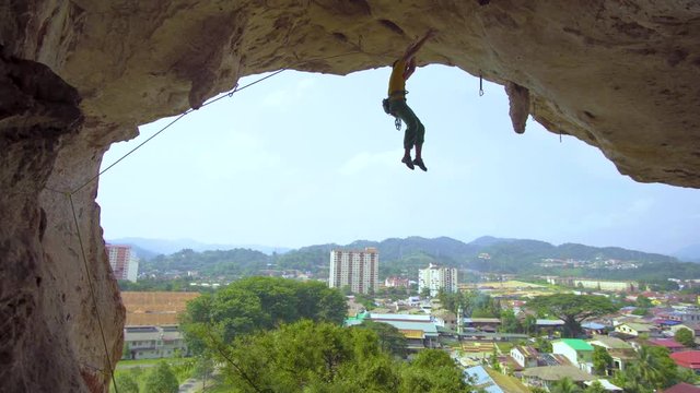 A man rock climbs under a cave opening upside don and swings to a stalactite at Batu Caves, Kuala Lumpur, Malaysia