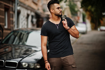 Awesome beautiful tall ararbian beard macho man in glasses and black t-shirt walking against business car.