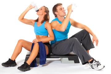 Fototapeta na wymiar Young man and woman sit back to back drinking clean water after fitness exercise against white background