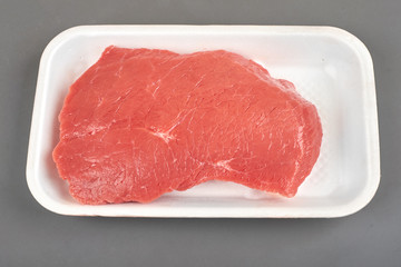 Fresh raw meat in a white tray on grey background.