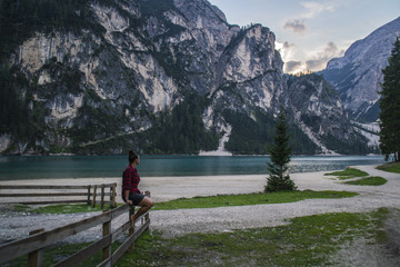 Fototapeta premium Young traveler girl sitting on the shore of Lago di Braies or Pragser Wildsee enjoying breathtaking mountain scene view and clear turquoise lake water in South Tyrol, Dolomites mountains, Italy. 