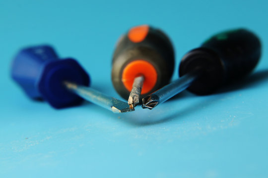 A two cross-point screwdrivers, one with black handle, second with orange-grey grip. Third tool is flat screwdriver