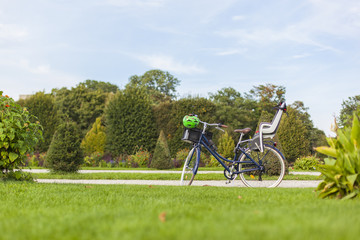 Obraz premium Vintage bicycle standing in Park with modern child bicycle carrier seat. Retro Fahrrad mit modernem Kindersitz und Fahrradhelm steht im Park.