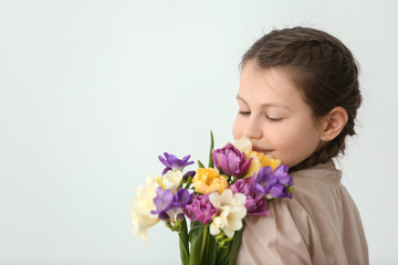 Little girl with bouquet of flowers on light background
