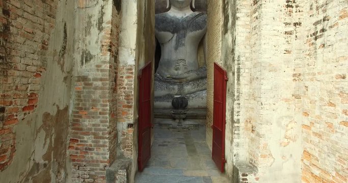 4K drone video footage gradually increasing altitude showing the big sitting Buddha statue at Wat Si Chum, a ruin site at Sukhothai Historical Park, a UNESCO world heritage site.