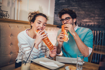 Cute young couple having a good time together and eating food in a coffee shop