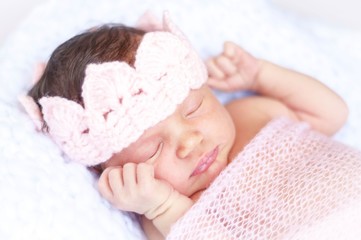 Obraz na płótnie Canvas Sweet sleeping tiny newborn princess with a pink crown wrapped in a soft blanket. Cute newborn baby sleeping stock image.